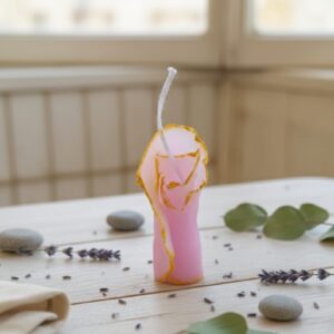 Pink handcrafted sculpture candle with golden edges placed on a wooden table for home décor.